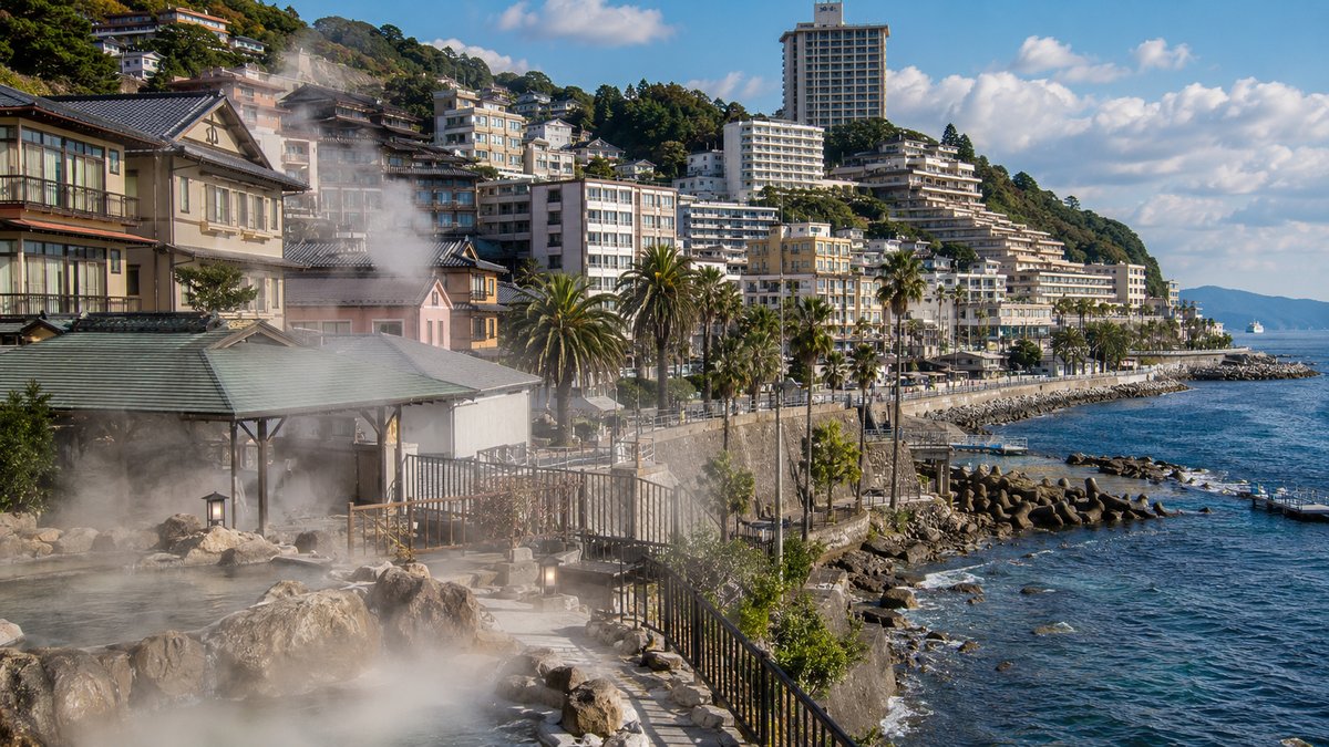 熱海温泉街の海岸沿いに湯気が立ち上る露天風呂と温泉宿の街並み