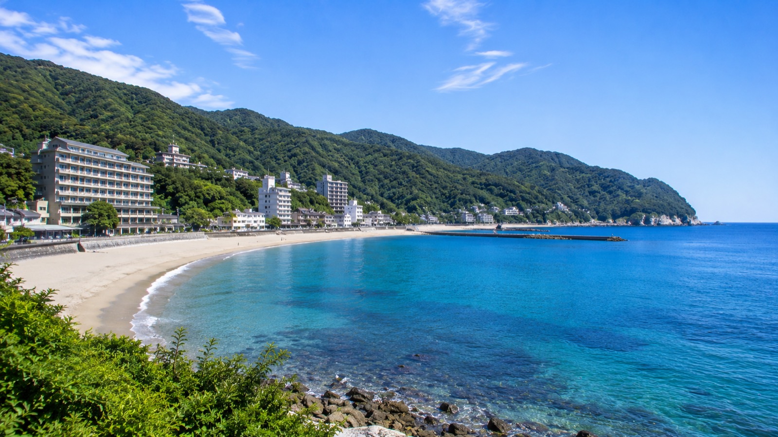 夏の晴れた日の伊東の海岸。弧を描く砂浜と青い海、海岸沿いに並ぶホテルや旅館